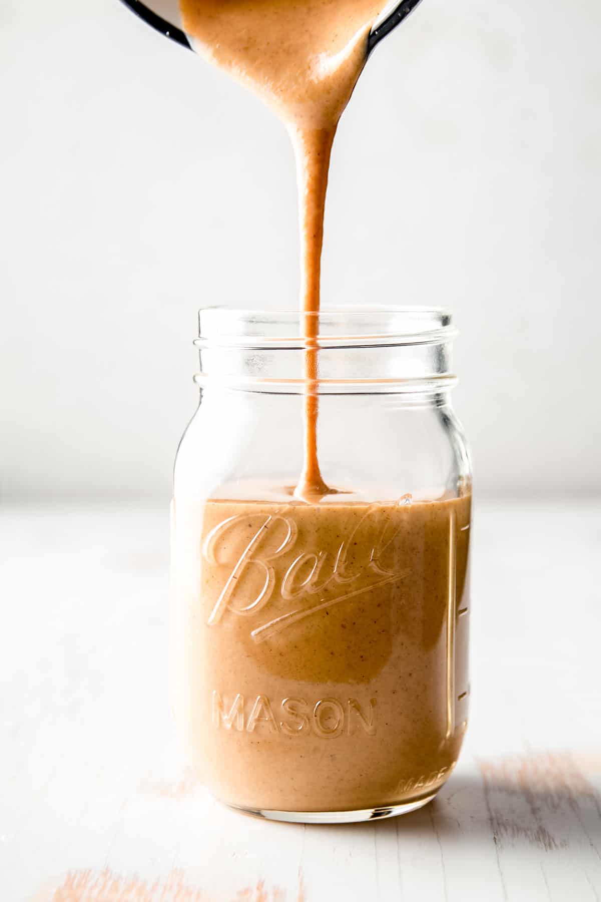 A stream of copycat Starbucks pumpkin spice sauce pouring into a mason jar.