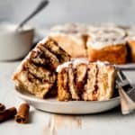 Cross section of a gluten free cinnamon roll on a plate with the rest of the rolls in the background.