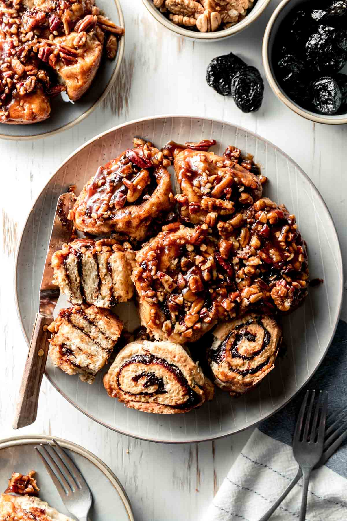 A plate full of gluten free sticky buns with gooey pecan caramel topping, some flipped over to show swirl of prune filling.