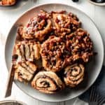 A plate full of gluten free sticky buns with gooey pecan caramel topping, some flipped over to show swirl of prune filling.