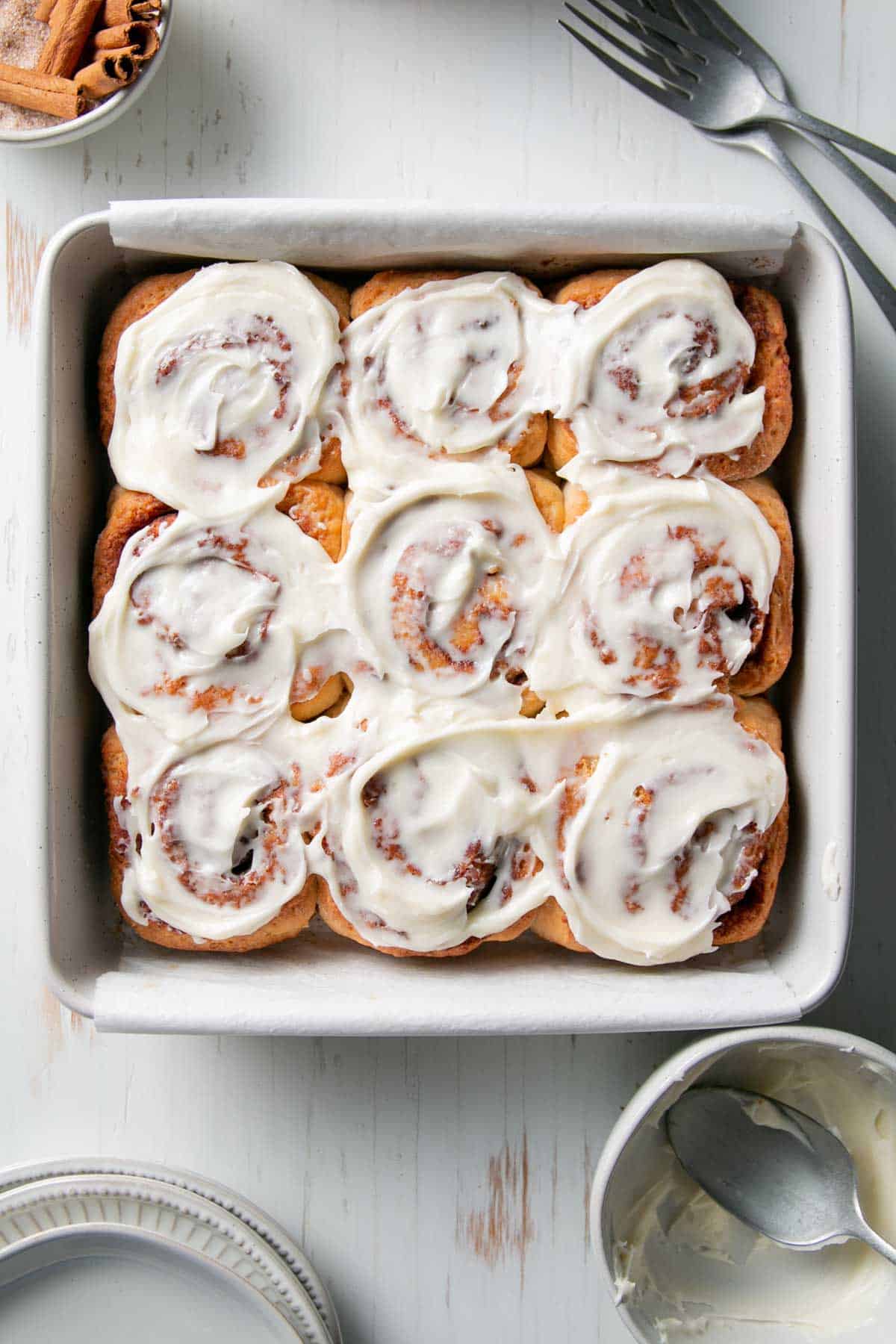 A square pan filled with baked cinnamon rolls topped with thick white frosting.