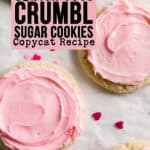Sugar cookies topped with swirly pink frosting scattered on crumpled parchment. Heart shaped sprinkles scattered around.