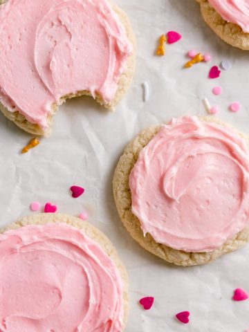 Gluten free crumble sugar cookies with swirls of pink icing are on crinkled parchment paper.