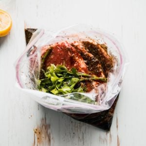 Steaks in zip top bag with marinade and parsley on top.