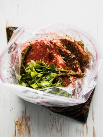 Steaks in zip top bag with marinade and parsley on top.