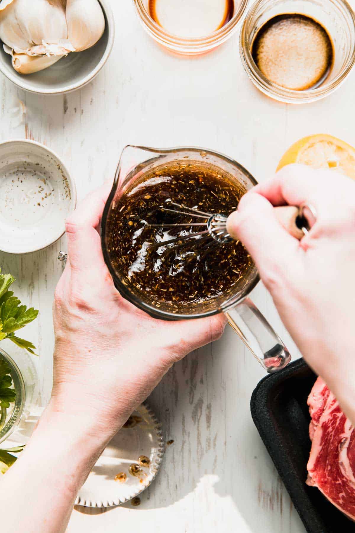 Hand whisking gluten free steak marinade in a glass measuring cup, surrounded by empty prep dishes.