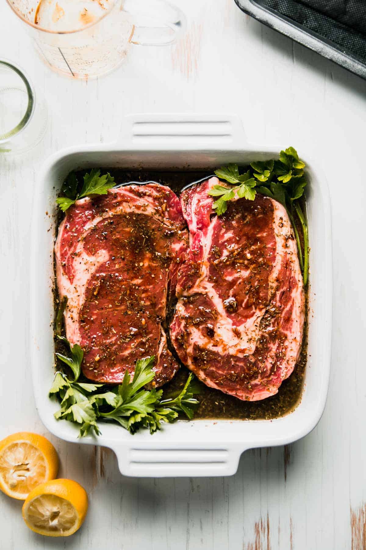 Steaks in square white dish with parsley nudged in corners, squeezed lemon halves next to dish.