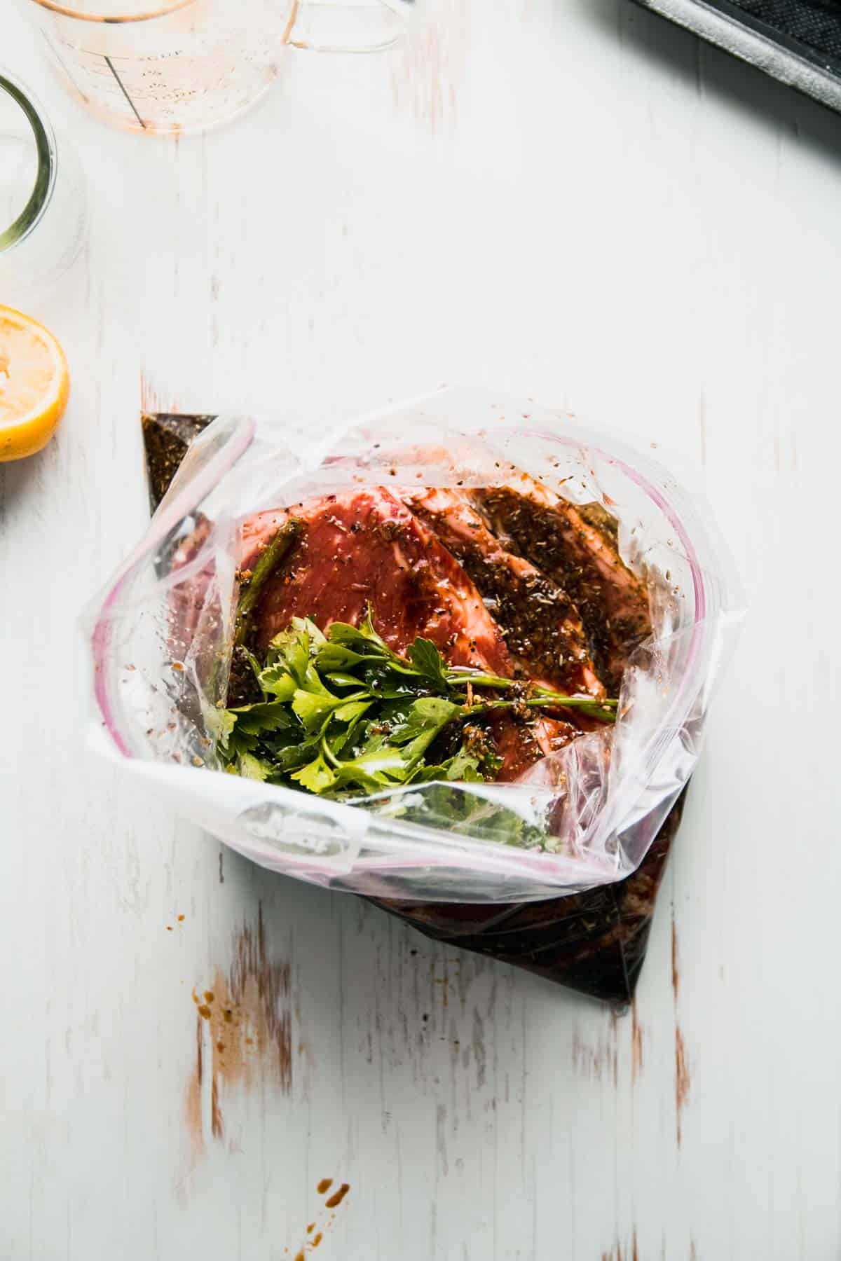 Steaks in zip top bag with marinade and parsley on top.