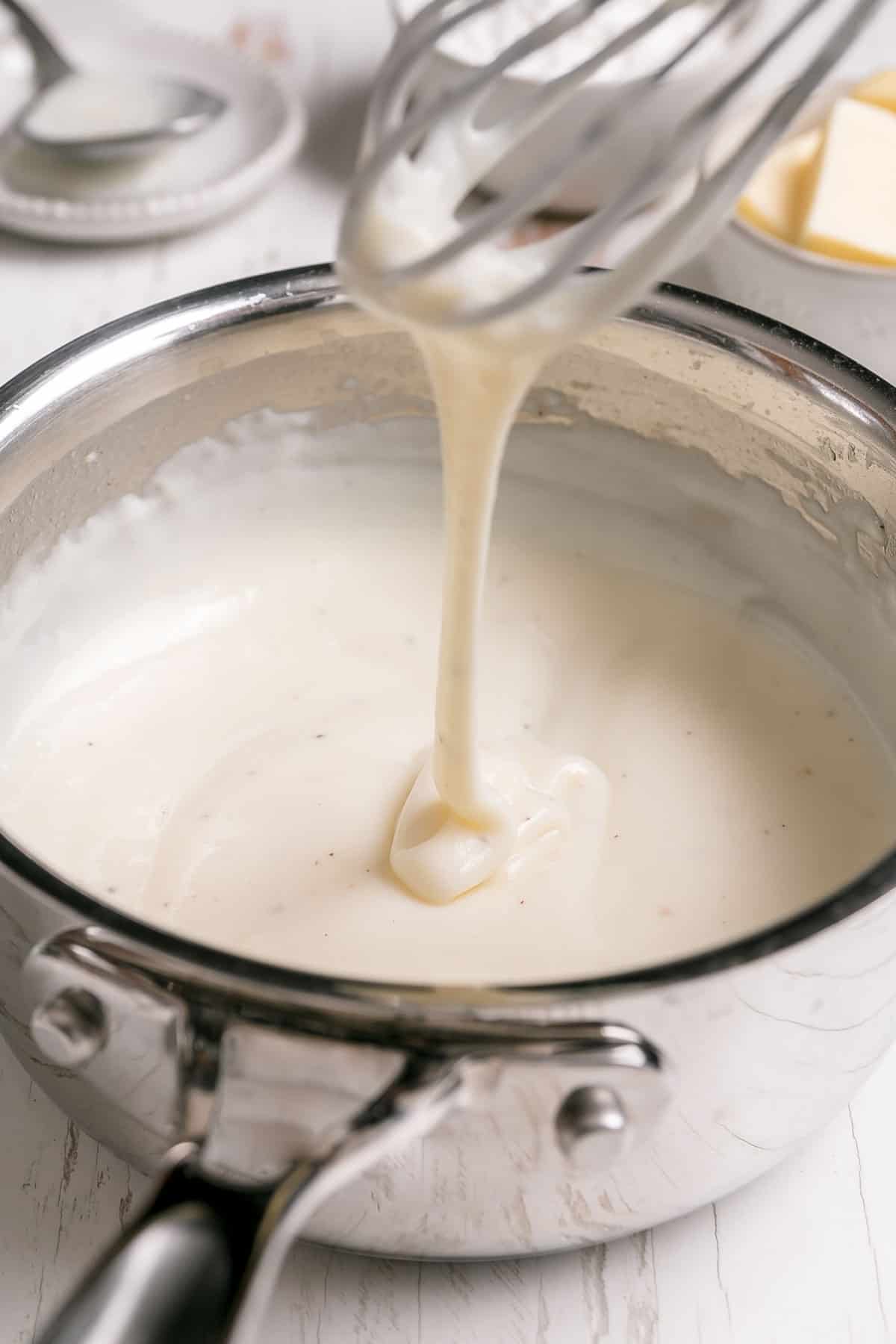 Gluten free white sauce dripping from a whisk back into a saucepan. 