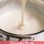 Gluten free white sauce dripping from a whisk back into a saucepan.