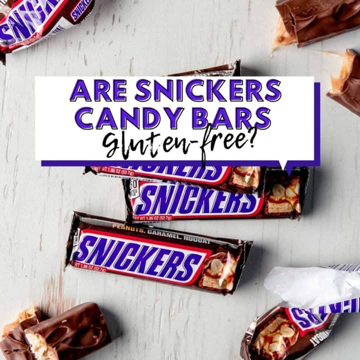 Snickers candy bars on white wooden surface, some unwrapped and broken apart.