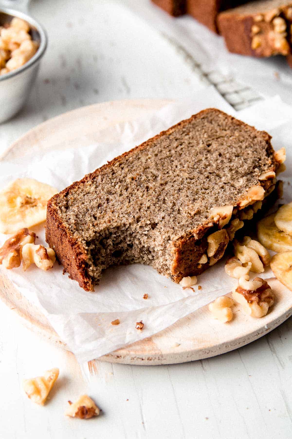 A slice of buckwheat banana bread with bite removed on small wooden plate.