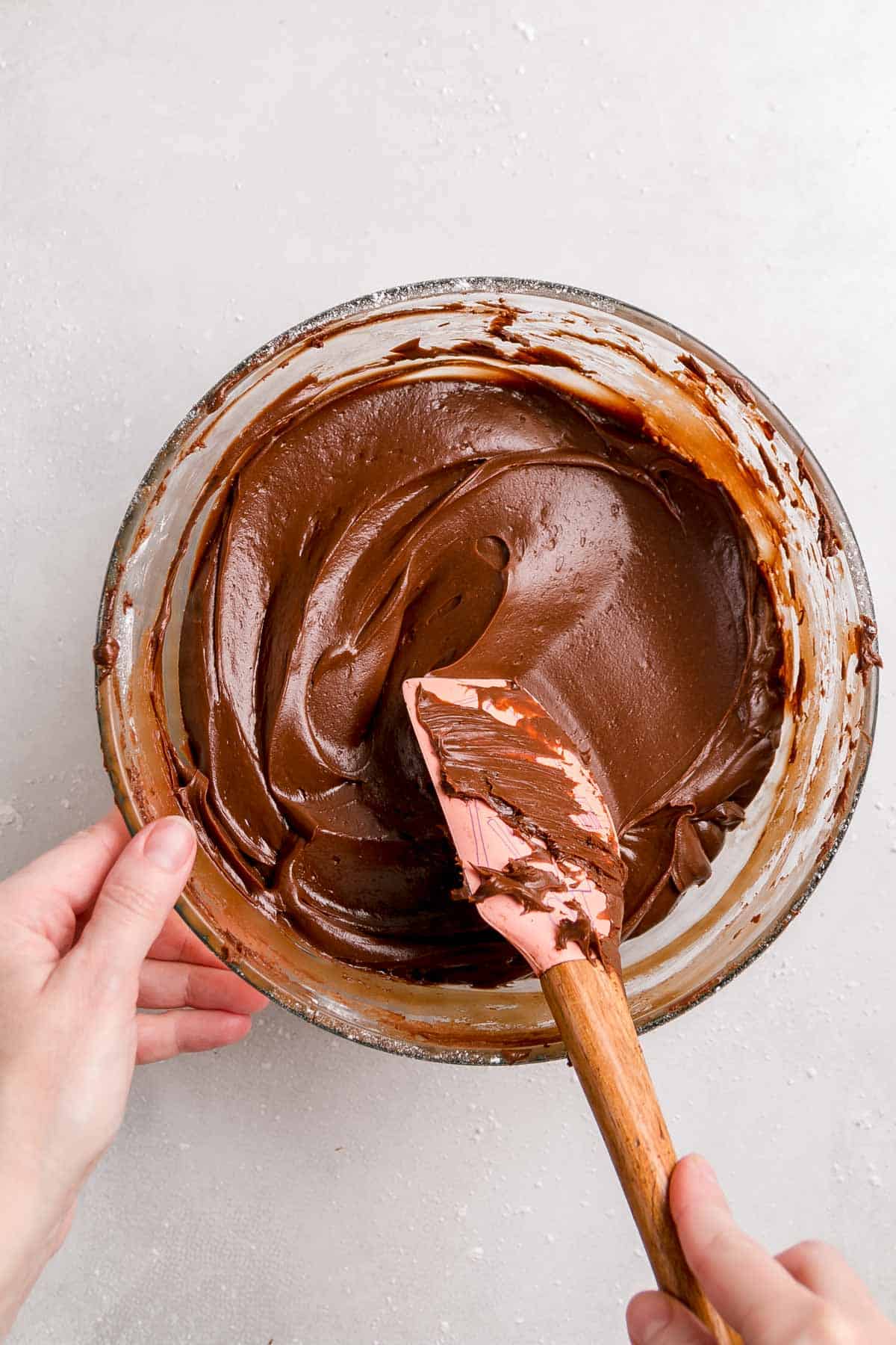 a bowl of chocolate icing with a pink spatula on white surface.