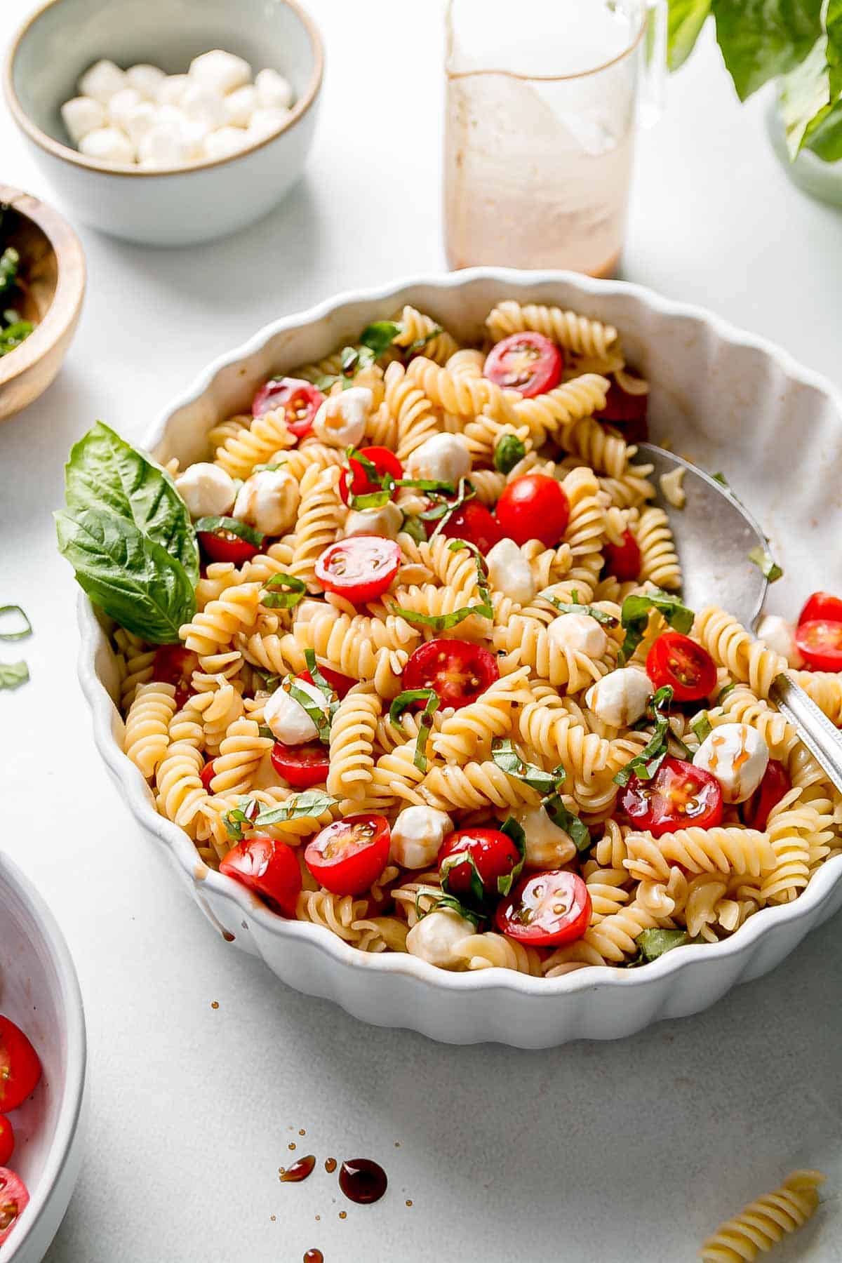 Gluten free caprese pasta salad in white dish next to extra ingredeints.