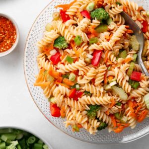 A big glass bowl filled with gluten free pasta salad with diced vegetables.