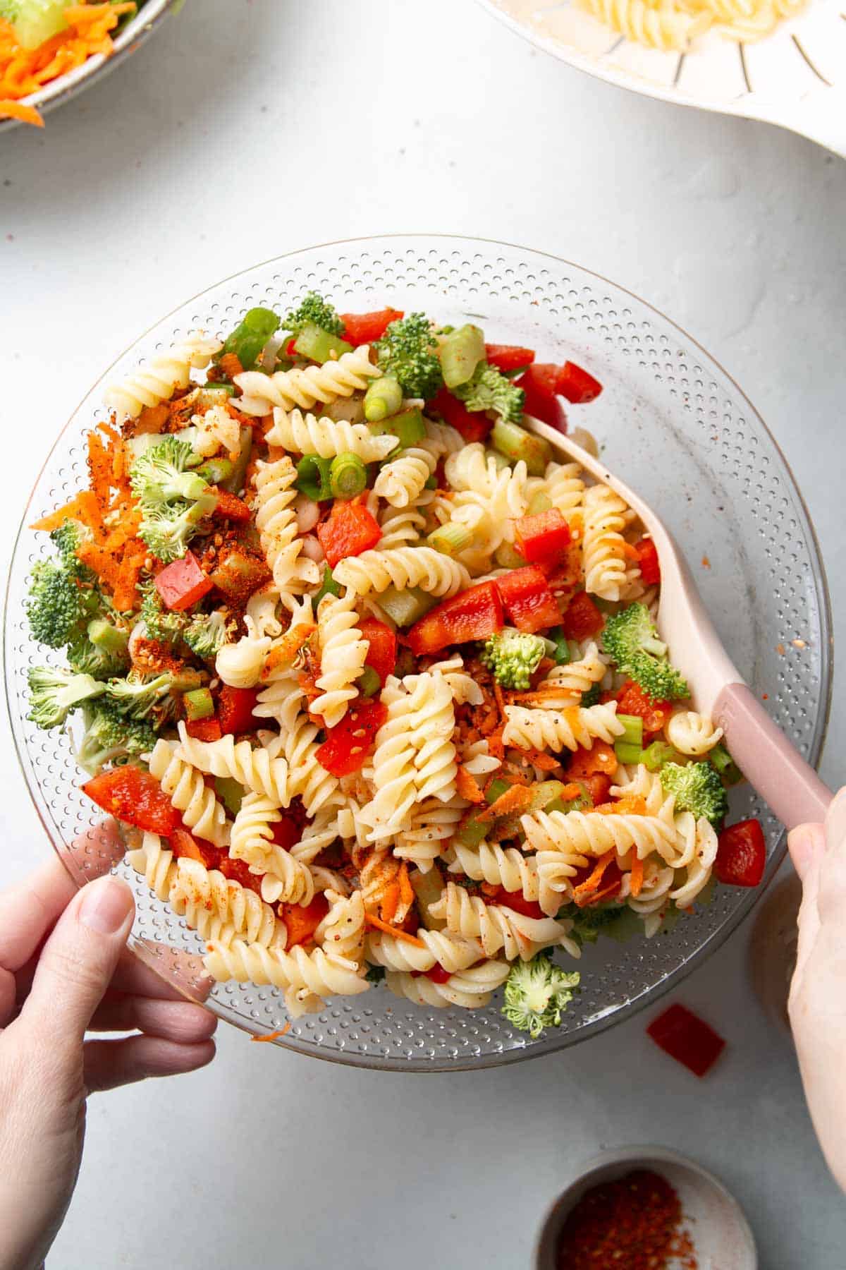Using slotted spoon to toss pasta salad in large bowl.