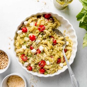 Gluten-free pesto pasta salad in a white dish with tomatoes and mozzarella pearls.