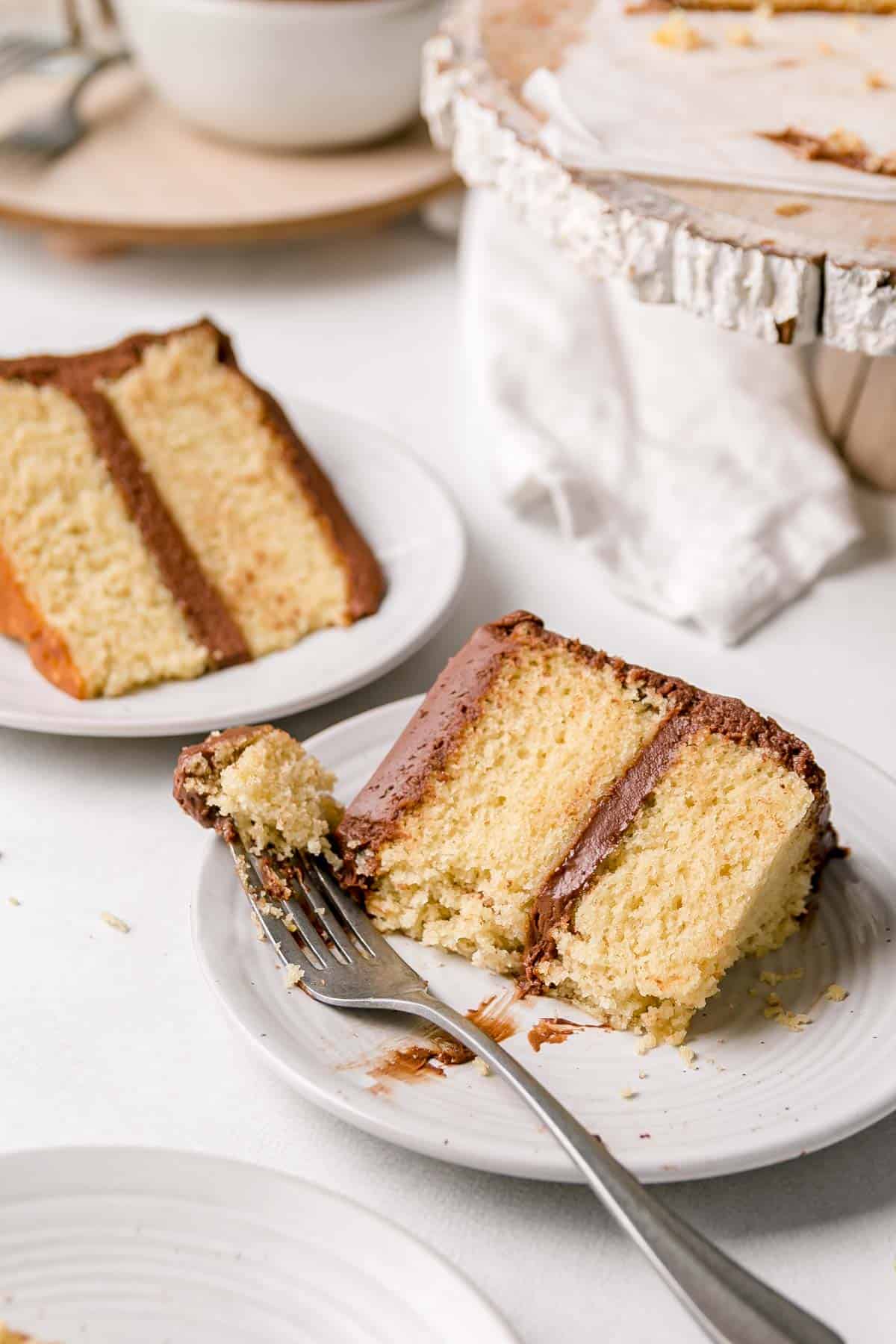 Gluten-free yellow vanilla cake slices on small plates, with bite on fork resting next to the slice. 