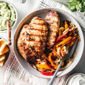 Mexican citrus marinated chicken breasts in a bowl with grilled bell peppers and onions.