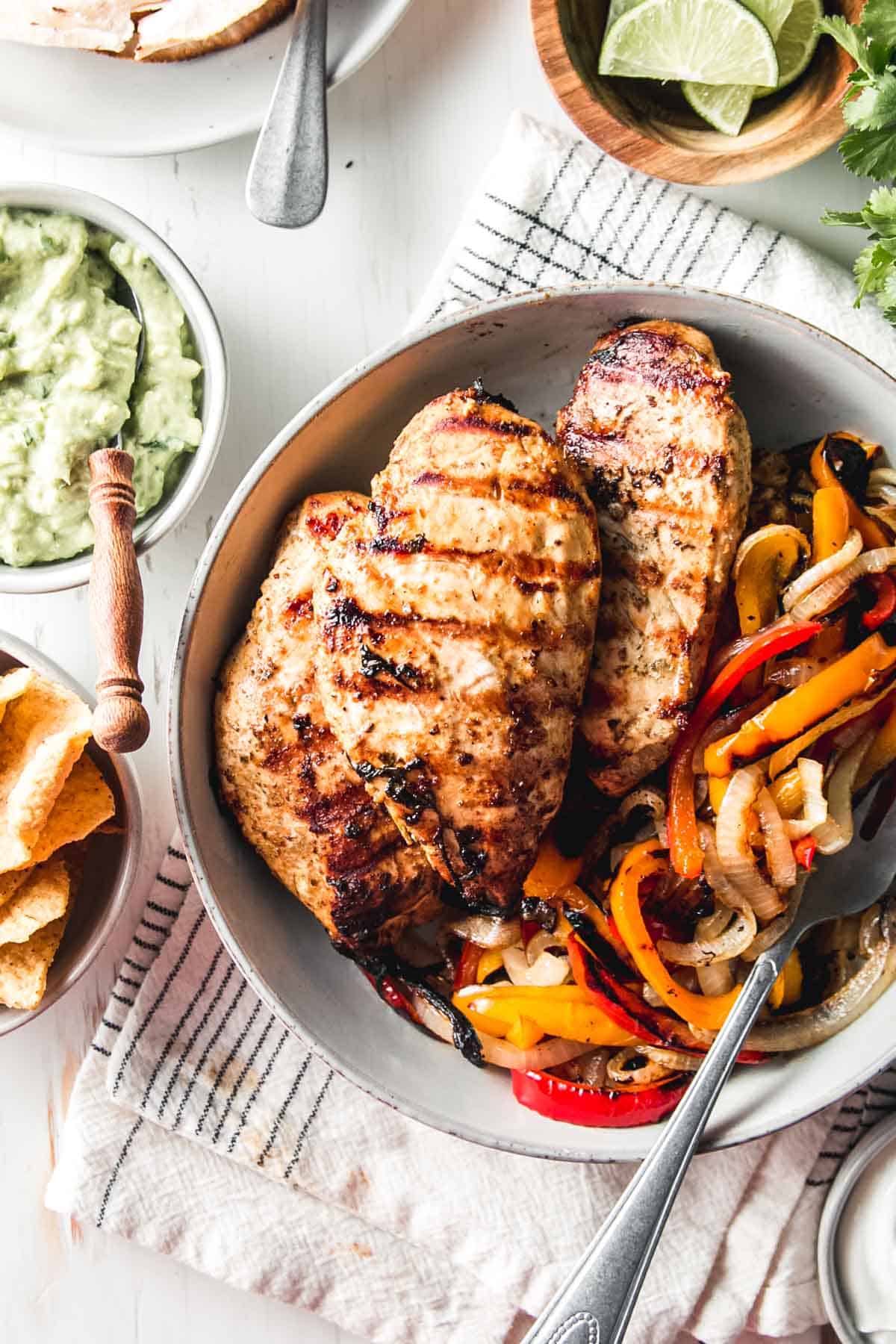 Mexican citrus marinated chicken breasts in a bowl with grilled bell peppers and onions.
