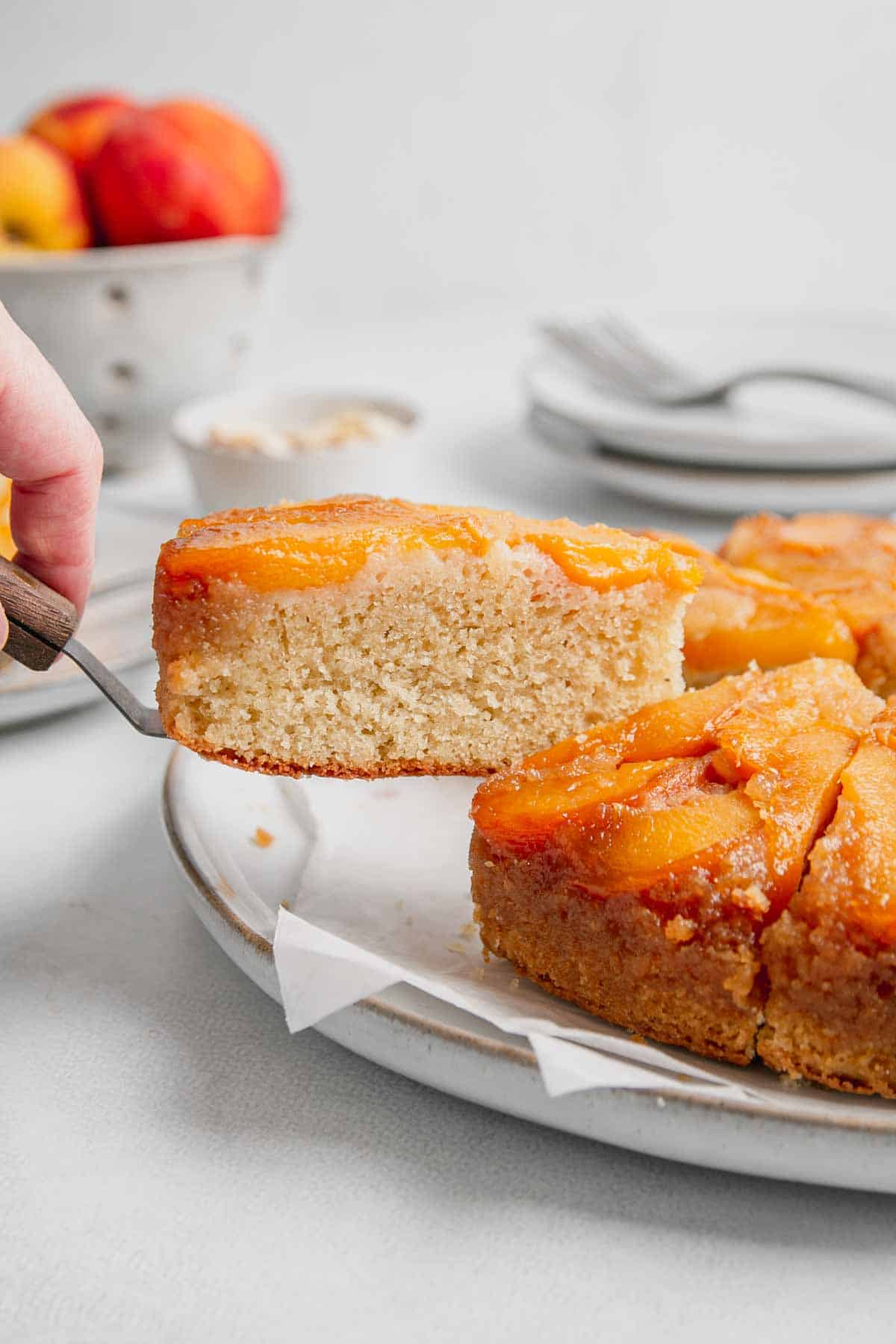 A slice of gluten free peach cake is lifted with a spatula from the rest of the cake.