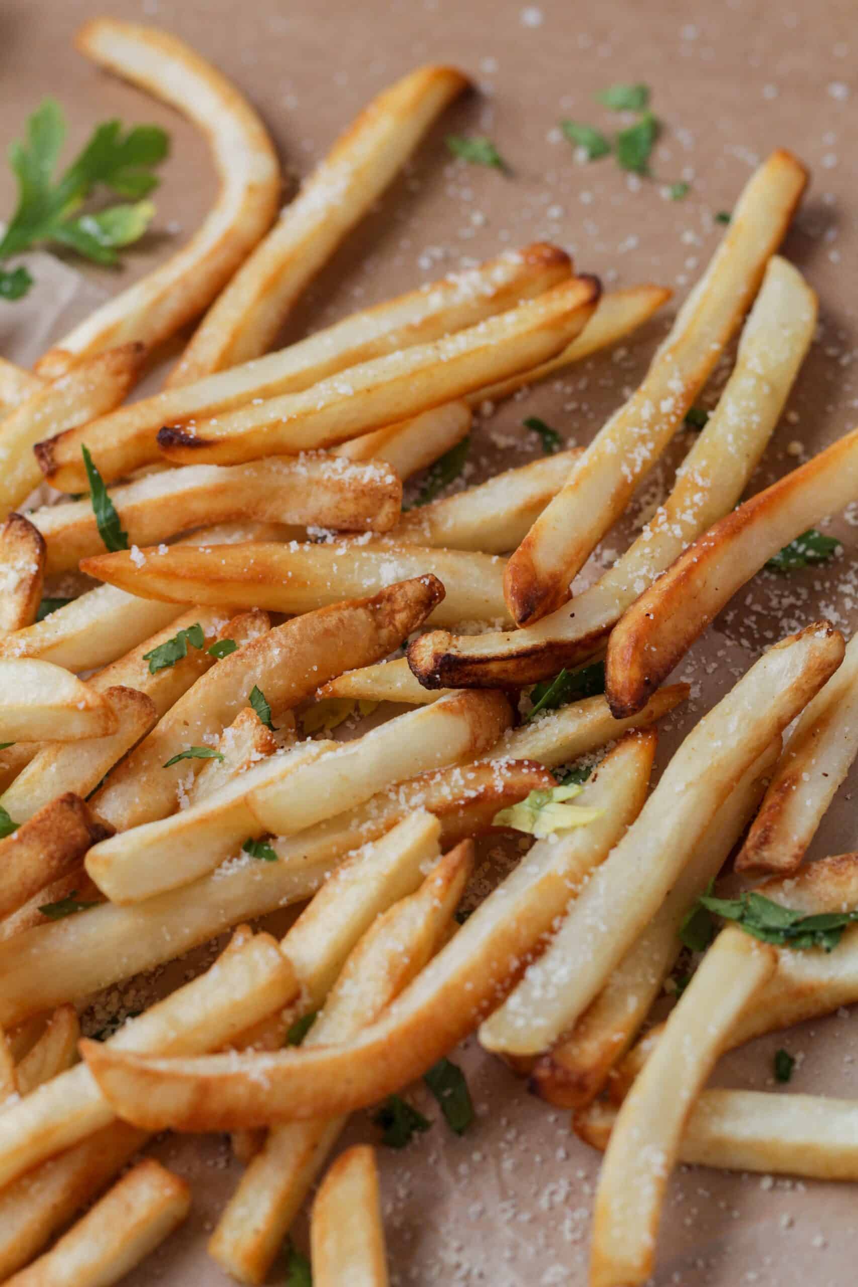 Golden brown French fries scattered on brown paper sprinkled with green parsley and parmesan cheese.