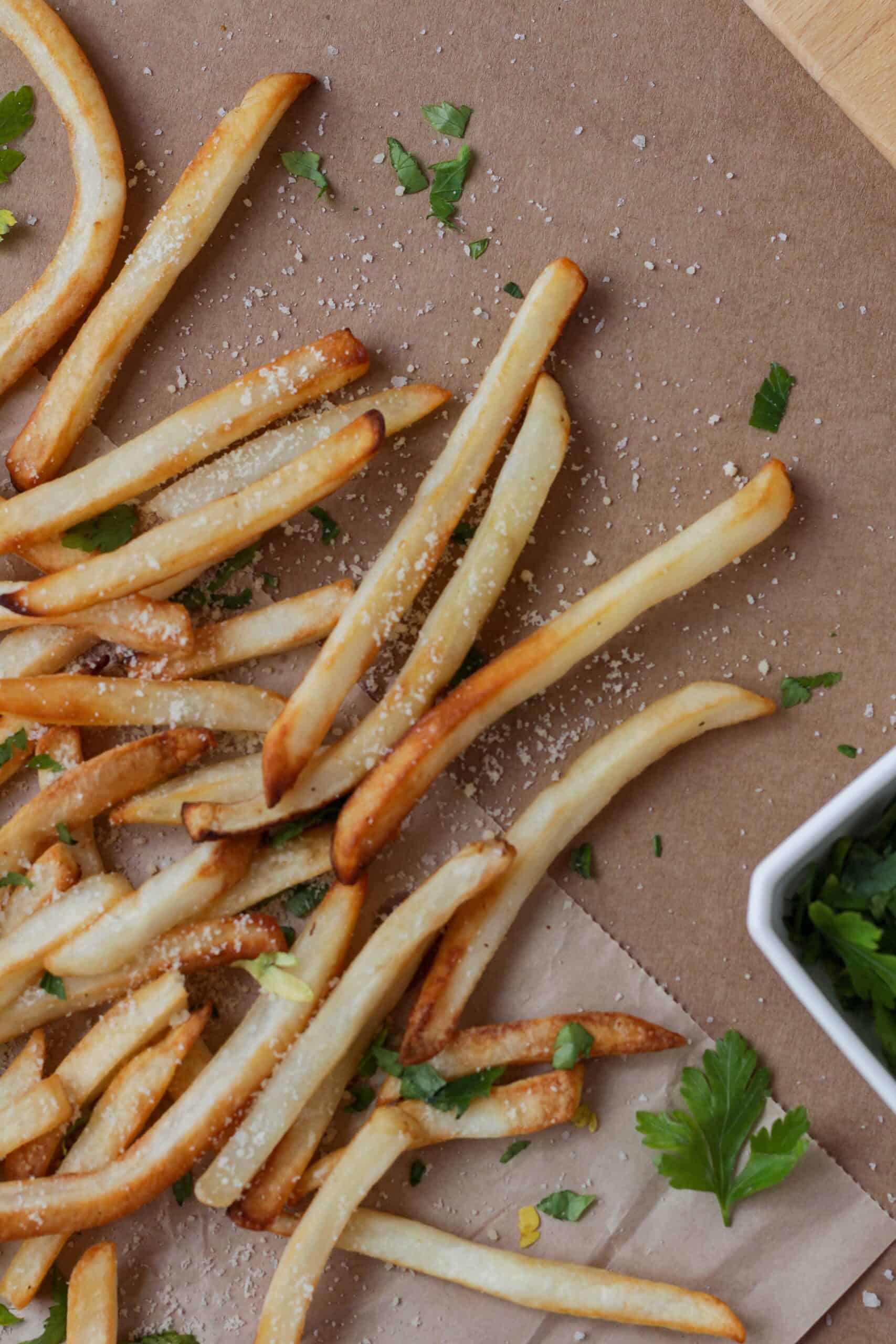 French fries are golden brown on parchment paper with parsley and parmesan.