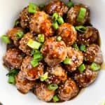 Meatballs in sauce sprinkled with sesame seeds and green onions.