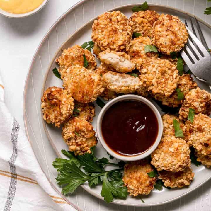 A plate of gluten free chicken nuggets with barbecue sauce and parsley for garnish.
