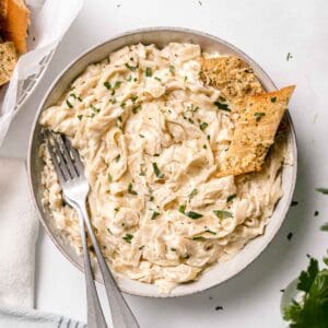 Gluten-free Fettuccini pasta in a large bowl with two forks and garlic bread to the side.