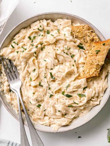 Gluten-free Fettuccini pasta in a large bowl with two forks and garlic bread to the side.