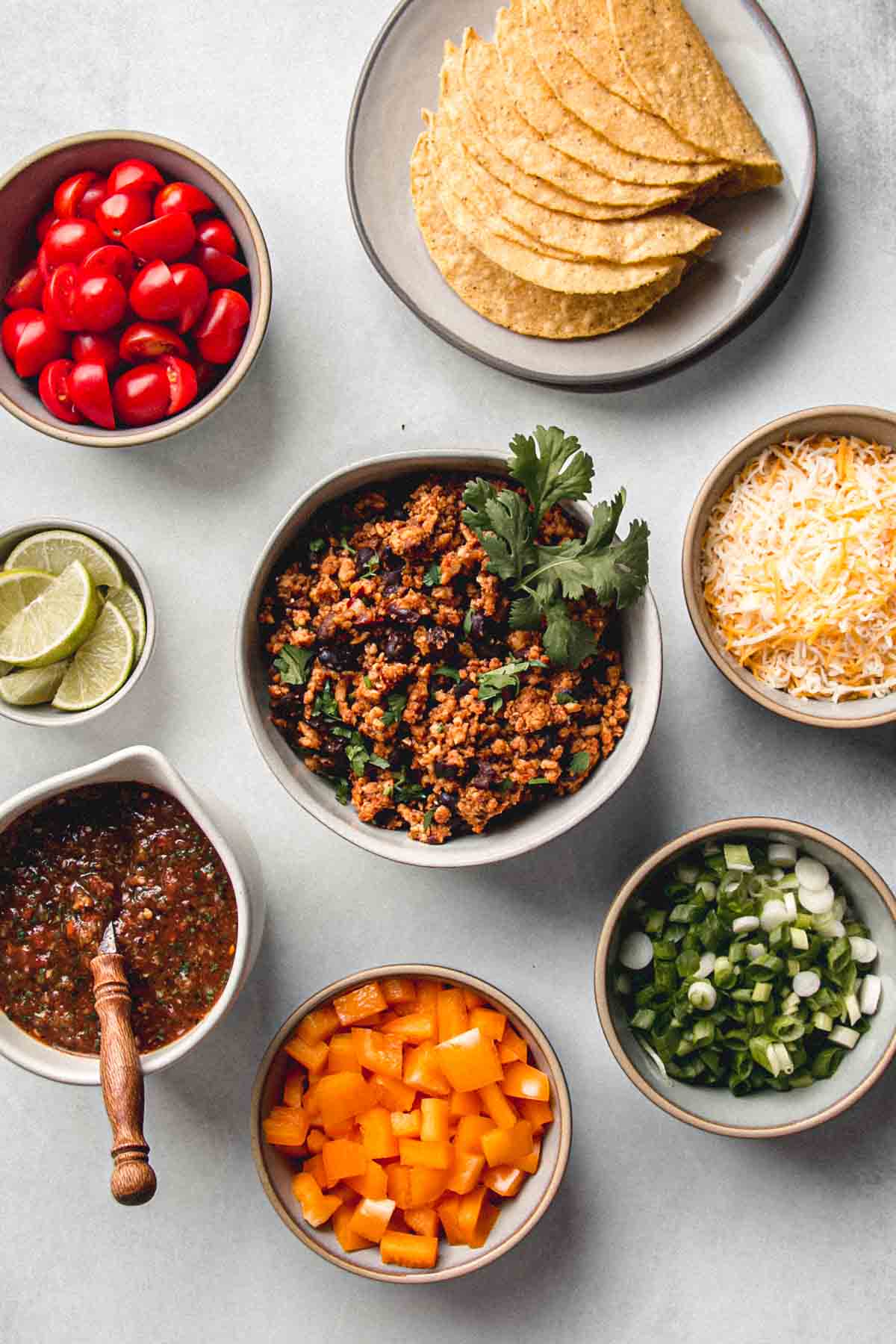 Ground chicken taco meat in a bowl topped with cilantro and surrounded by bowls of taco fixings.