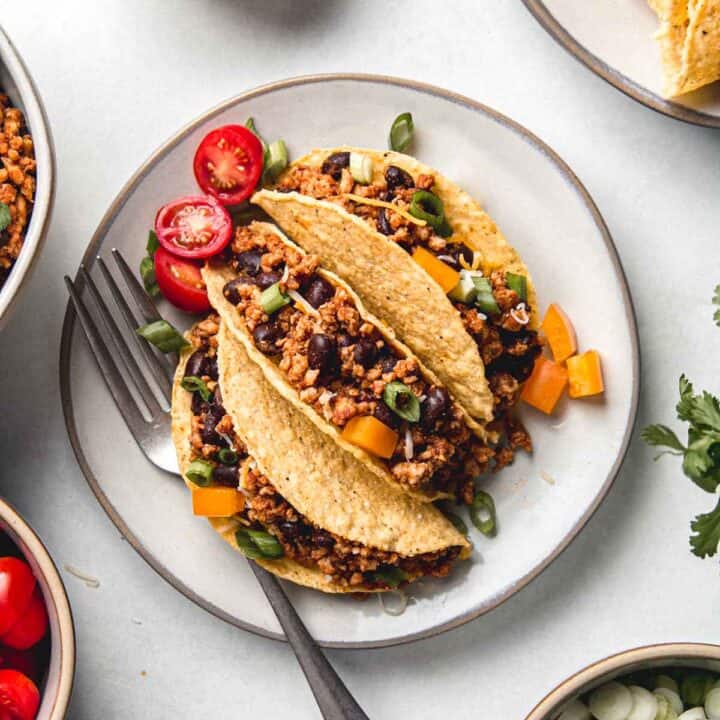 Three gluten-free ground chicken tacos on small plate with sliced cherry tomatoes and diced bell pepper.