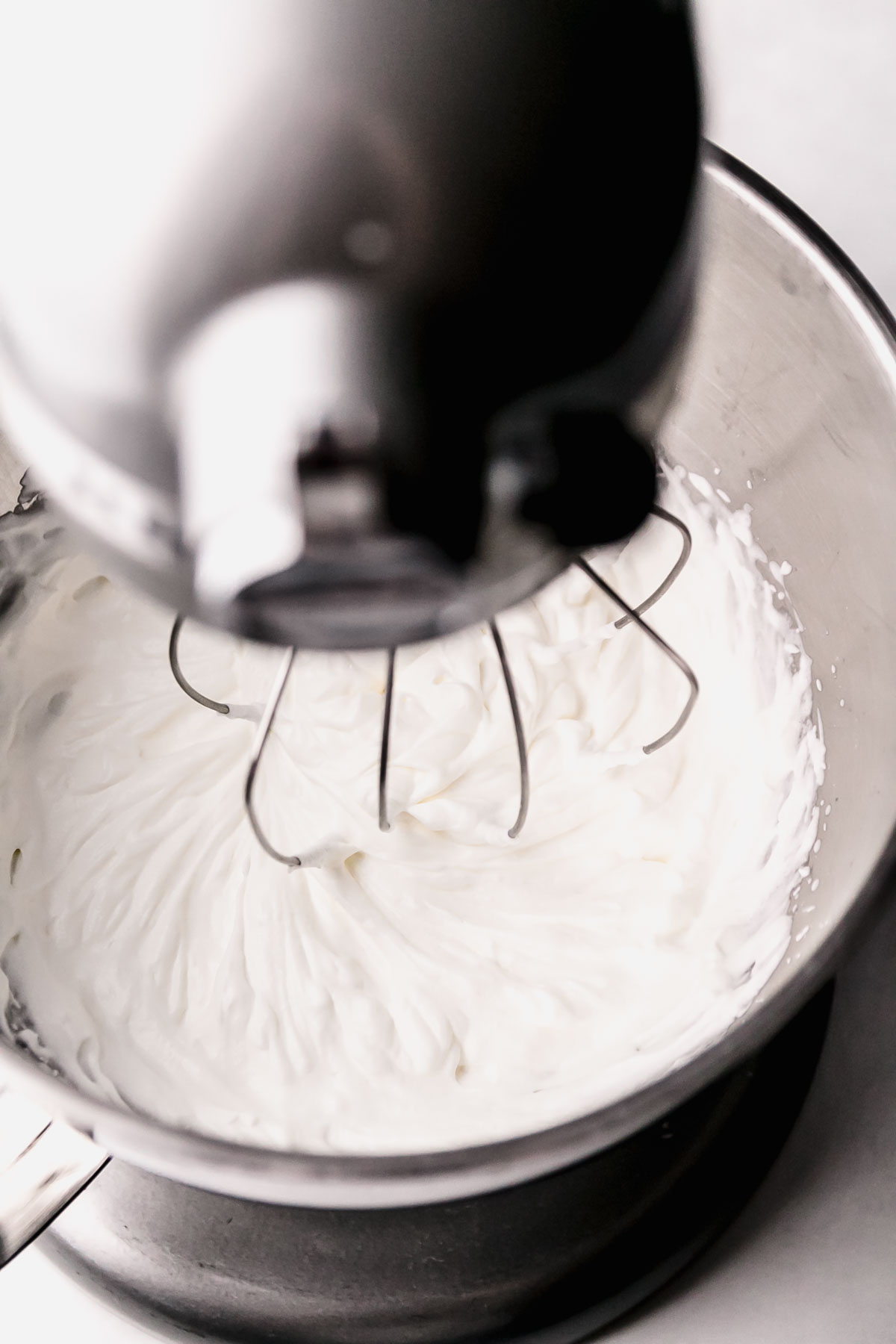 Whipped cream in stand mixer bowl with whisk attachment.