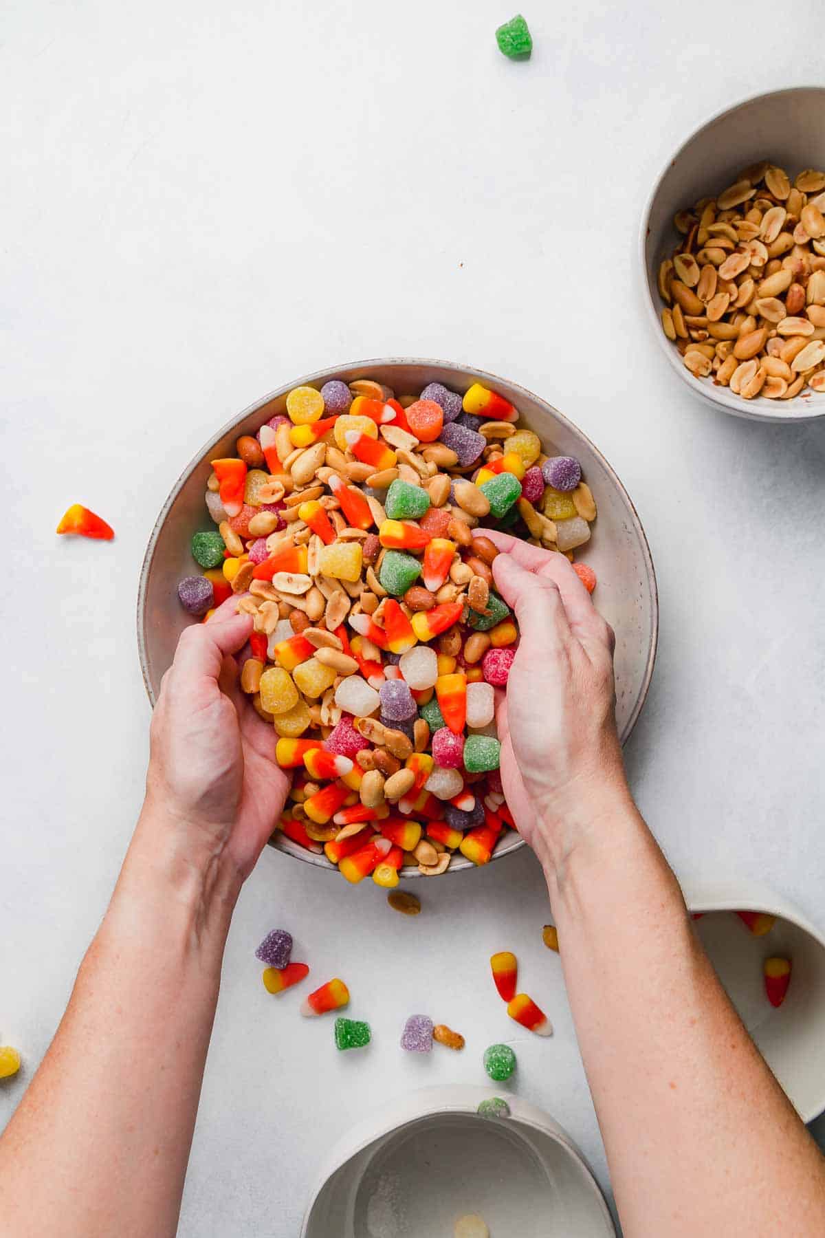 Hands mixing the candy corn snack mix together.