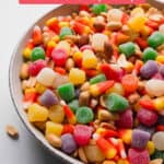 A bowl full of candy corn mixed with peanuts and spice drops. Some spilled out the sides.