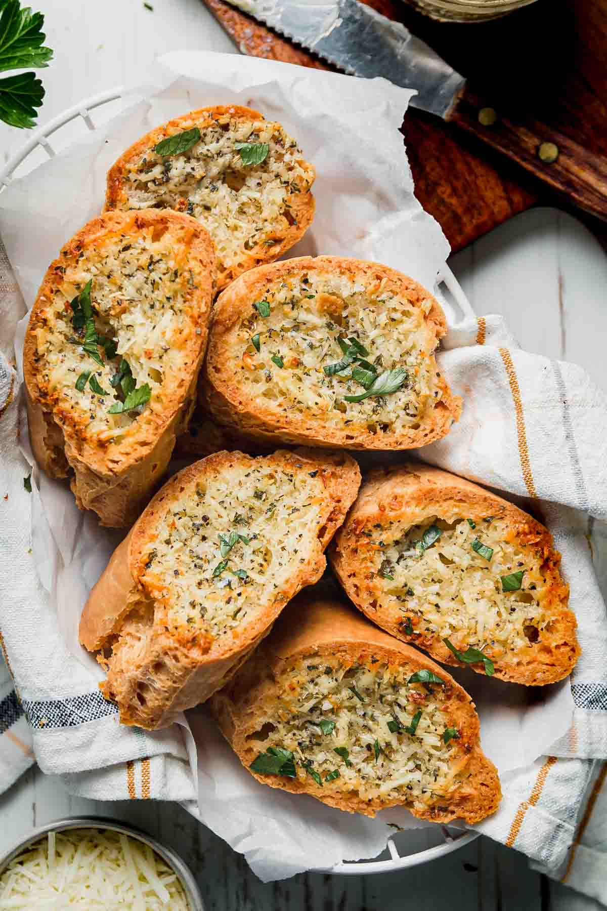 A basket lined with a towel filled with slices of garlic bread garnished with fresh parsley. 