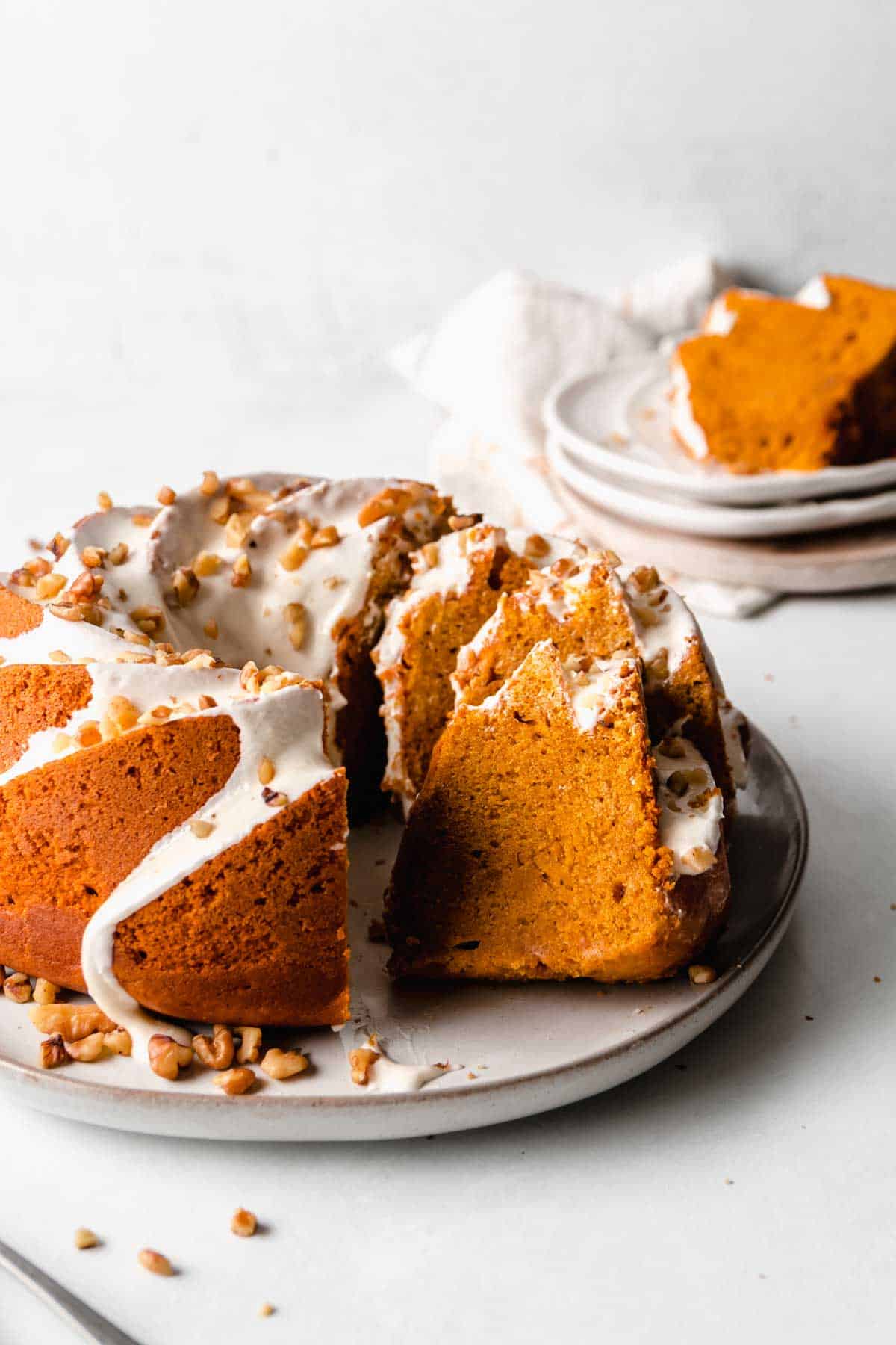 Partially sliced pumpkin bundt cake is orange with white icing, slices rest against the rest of the unsliced cake.