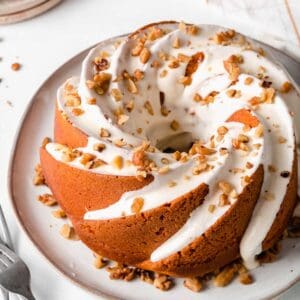 Gluten-free pumpkin bundt cake with frosting dripping down the sides, sprinkled with chopped walnuts.