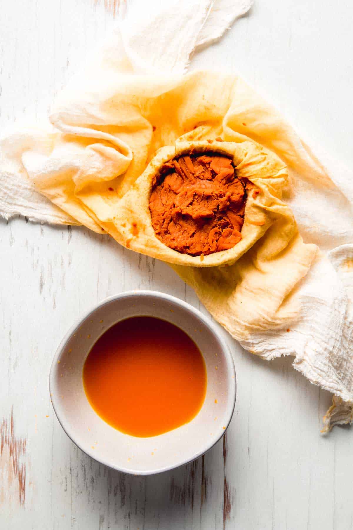 Pumpkin puree in orange stained cheesecloth next to a small bowl of pumpkin juice.