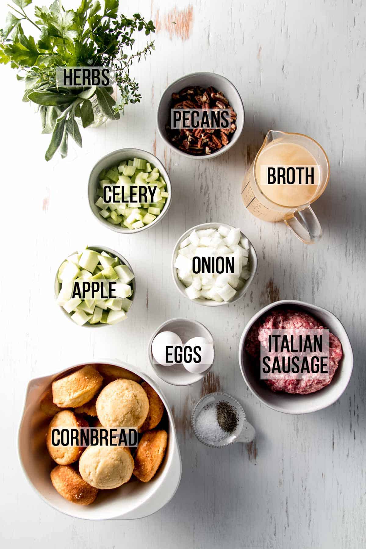 Ingredients for gluten-free cornbread stuffing measured out in bowls on white wooden surface. 