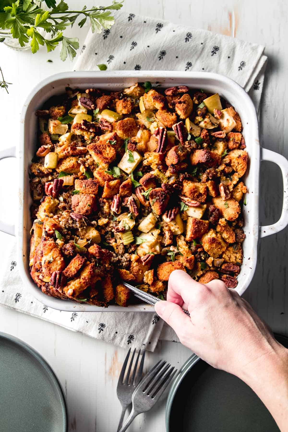 Hand removing a scoop of cornbread stuffing from casserole dish.