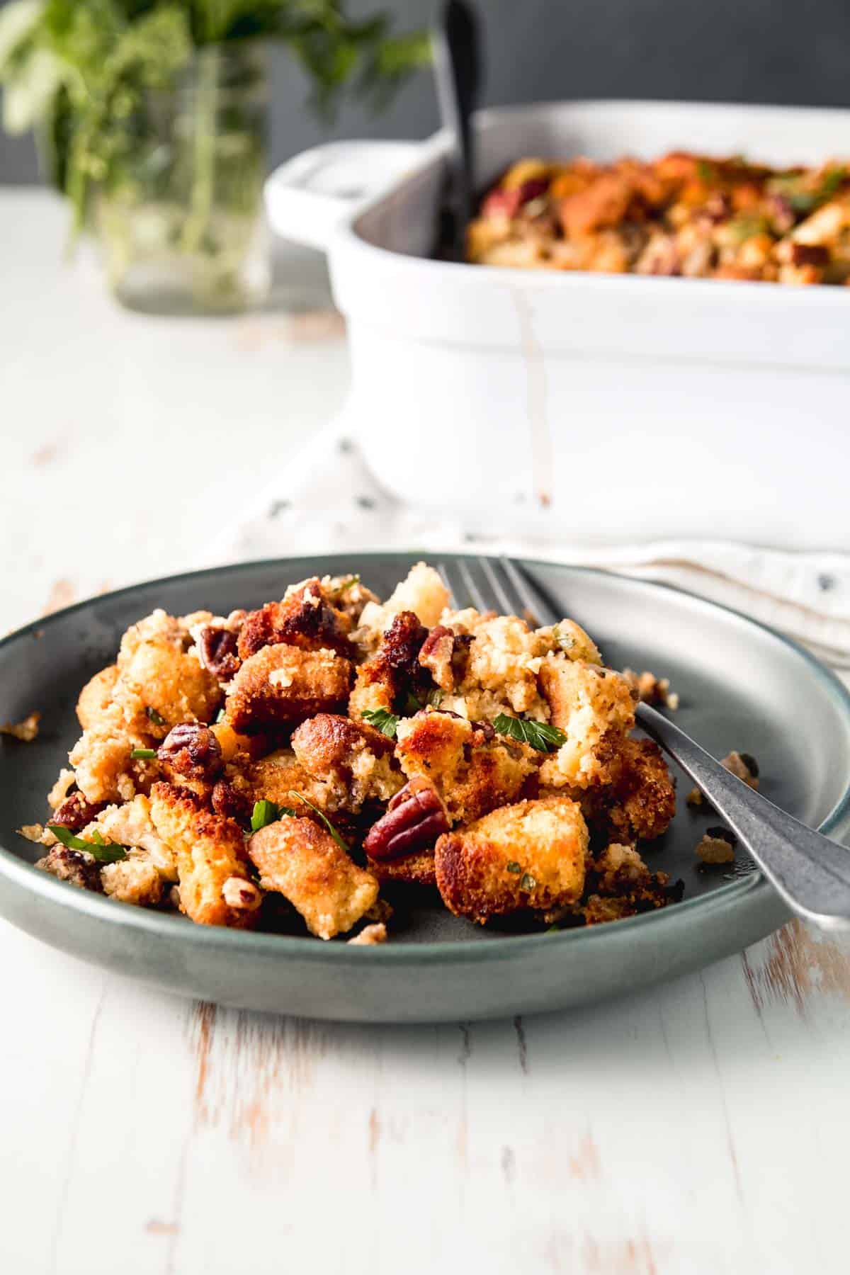 A scoop of stuffing on a green plate sprinkled with pecans and fresh herbs.