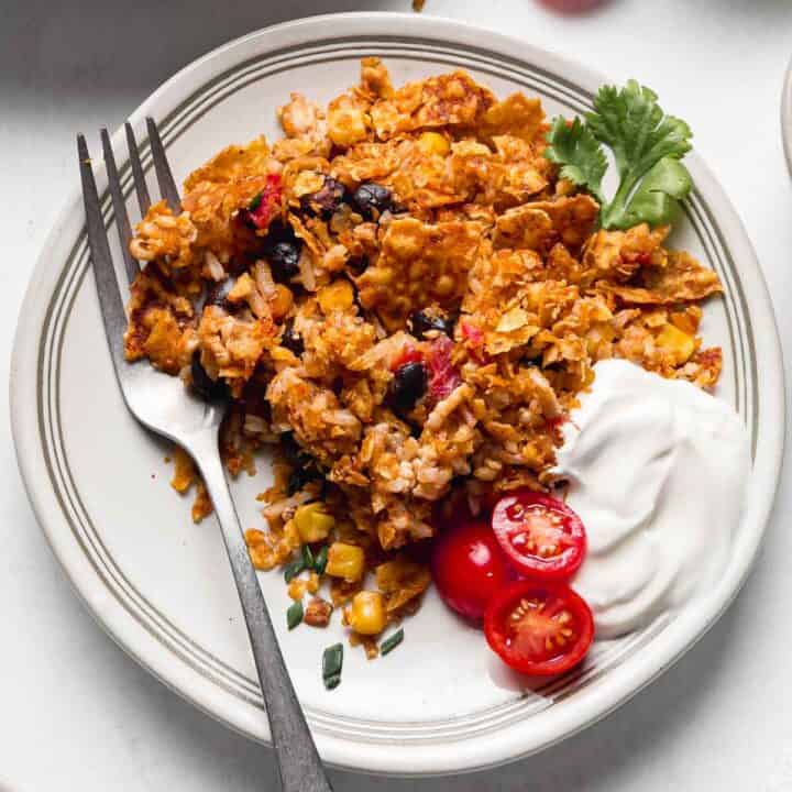 Chicken taco casserole on plate with sliced tomatoes and sour cream.