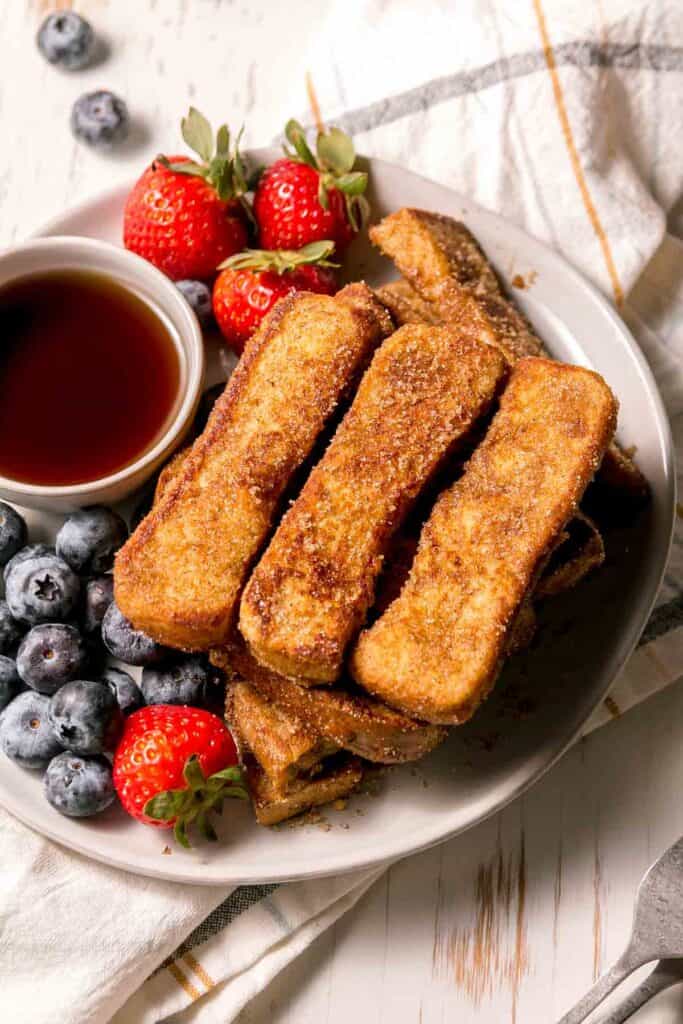 A plate of gluten free pancakes, a bowl of baked oatmeal gluten free, and a gluten free breakfast sandwich on a wooden table.