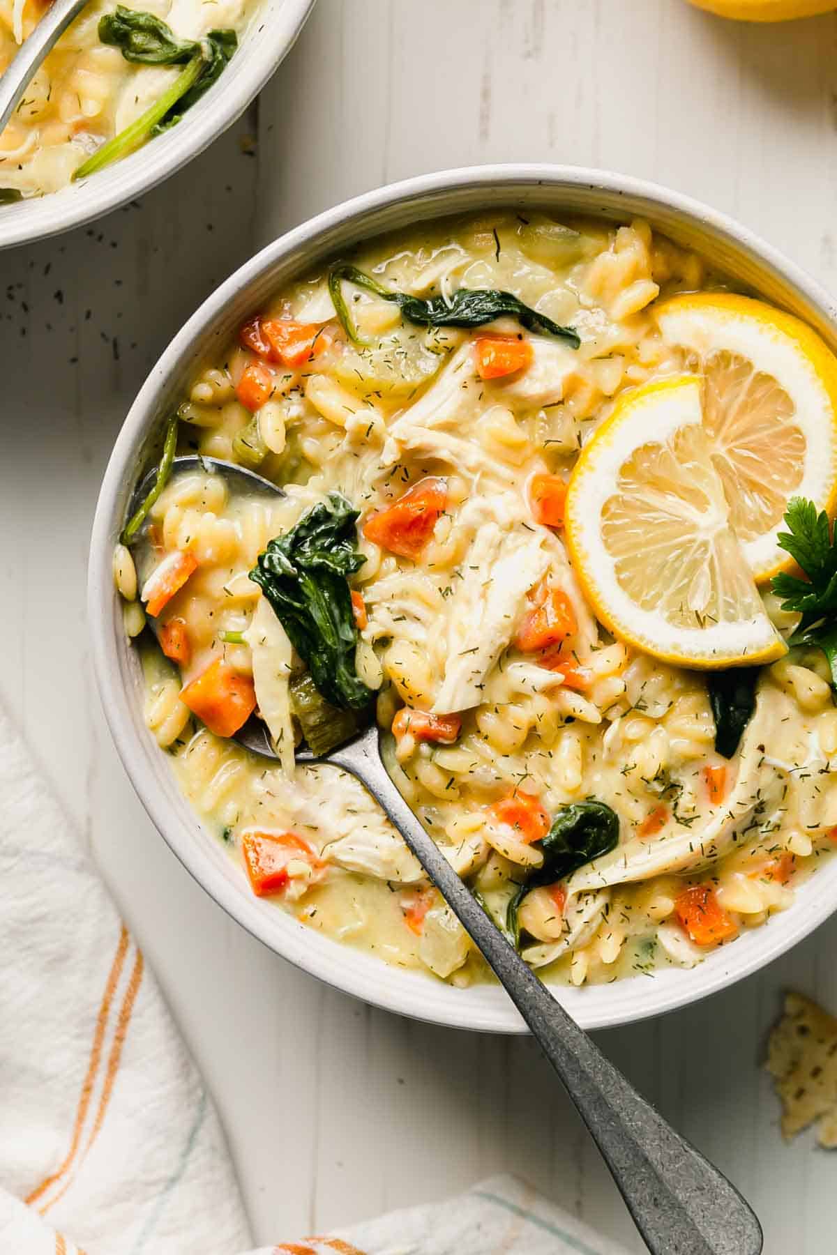 Lemon chicken orzo soup in a bowl with wilted spinach, garnished with lemon slices and fresh parsley. 