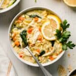 Gluten free lemon chicken orzo soup in a bowl with lemons slices and parsley for garnish.