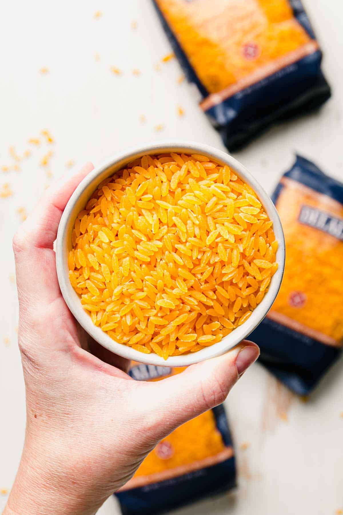 A small bowl of uncooked orzo held up by a hand.