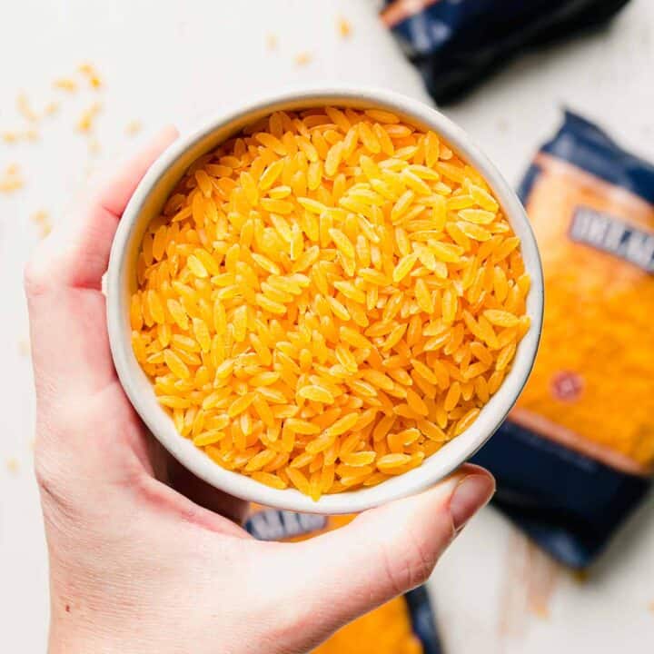 A hand holding a small bowl full of uncooked gluten-free orzo.
