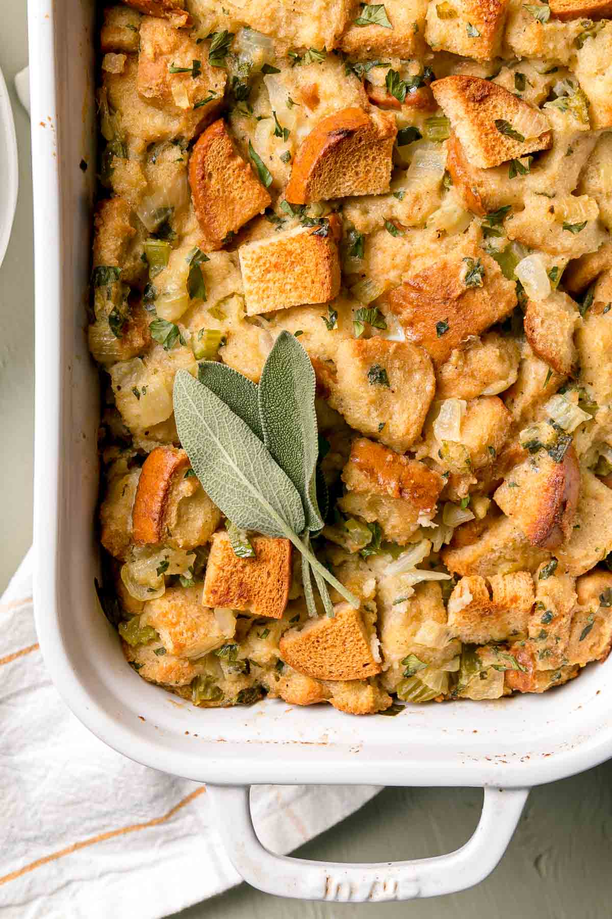 Close up image of baked stuffing showing golden brown toasted tops of bread cubes, garnished with sage leaves. 